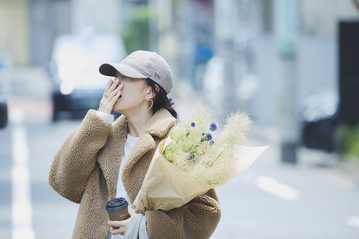 若い女性が花束とコーヒーを持って通りを歩いている様子